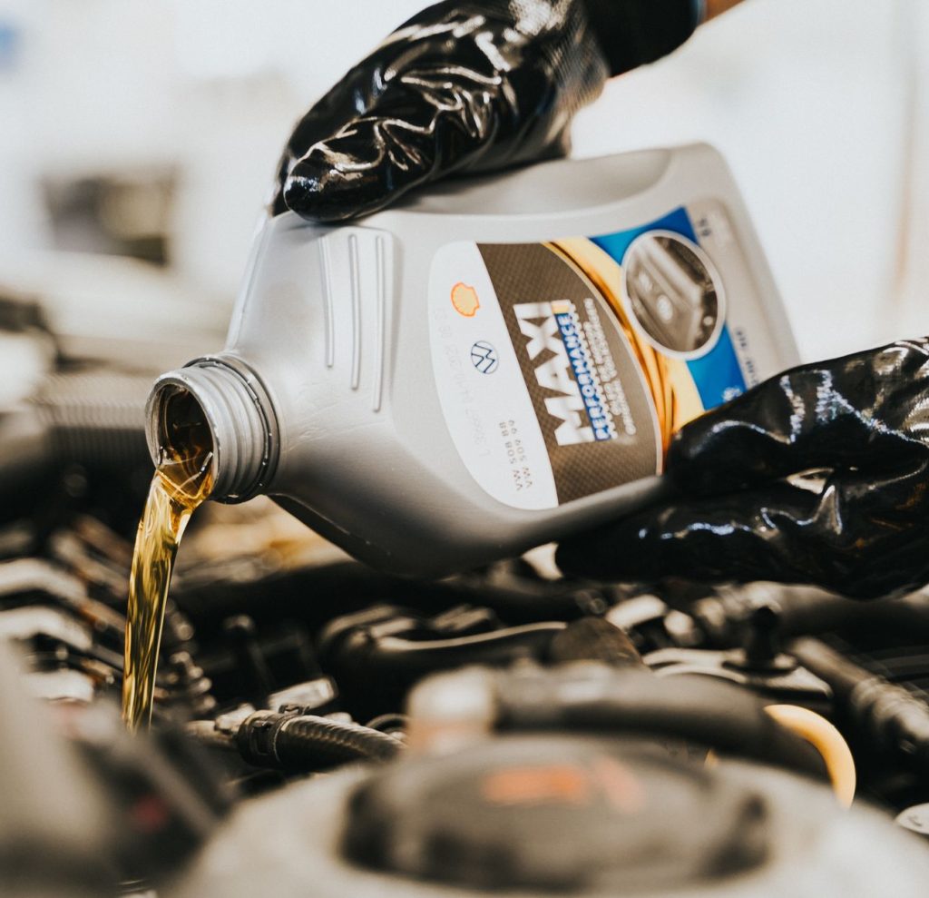 Close-up of a mechanic pouring engine oil into a car engine, highlighting maintenance work.